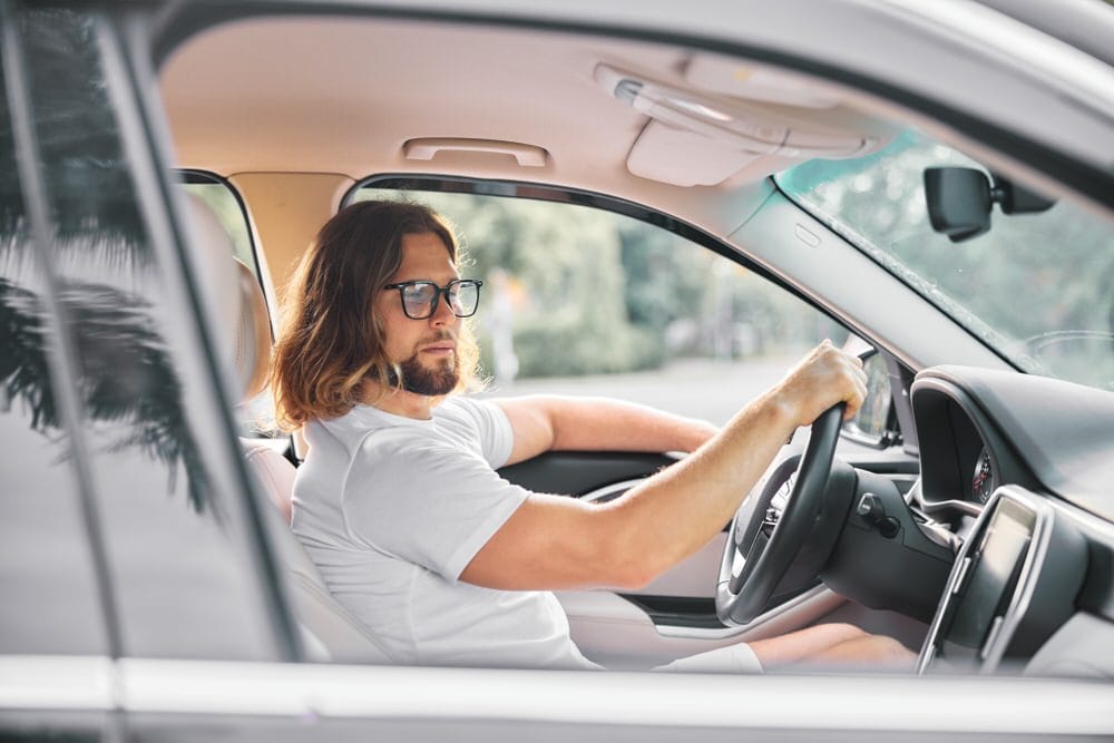 Bărbat șarmant la volan, reprezentând un iubit pasionat de mașini pentru care un cadou personalizat auto este ideal.